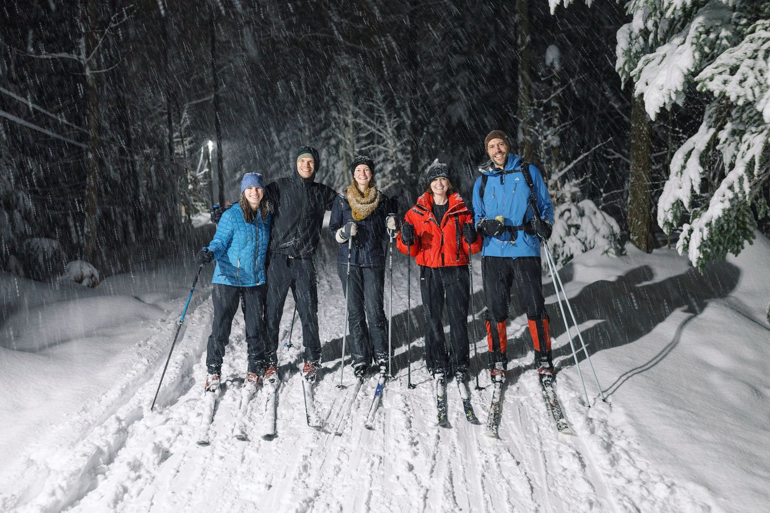Group of winter sports enthusiasts posing together on a snowy forest trail with ski equipment.