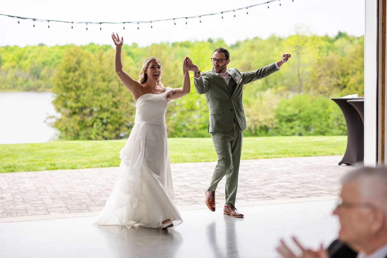 Bride and groom celebrate their first dance at an outdoor wedding venue with scenic lake and greenery backdrop.