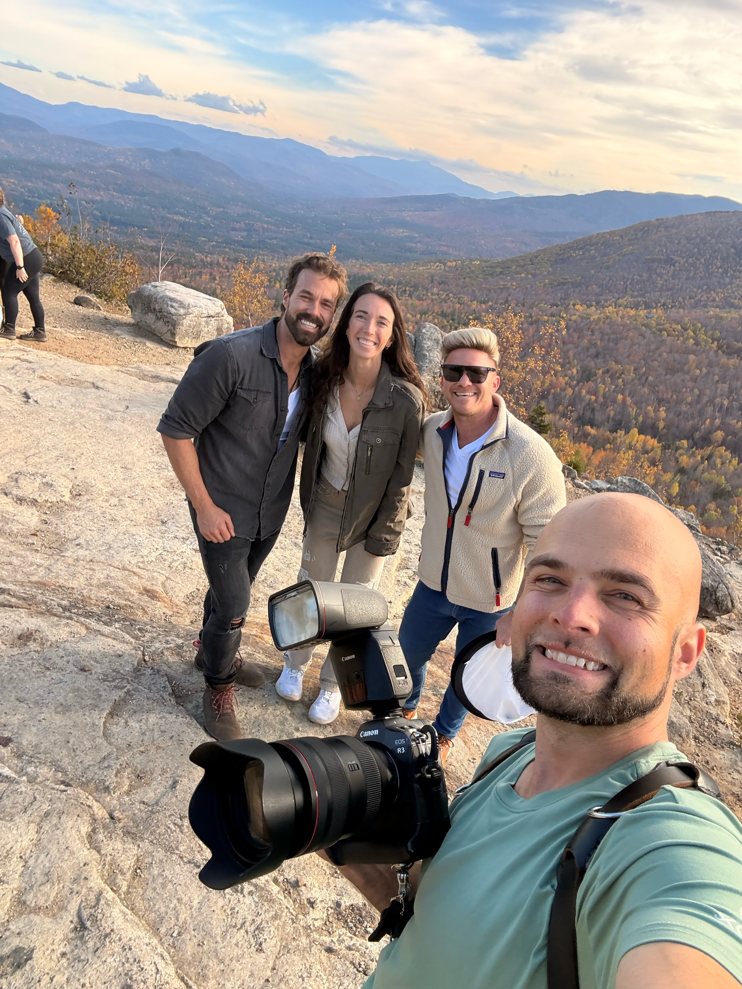Group taking a selfie on a mountain summit during autumn with colorful foliage in the background.