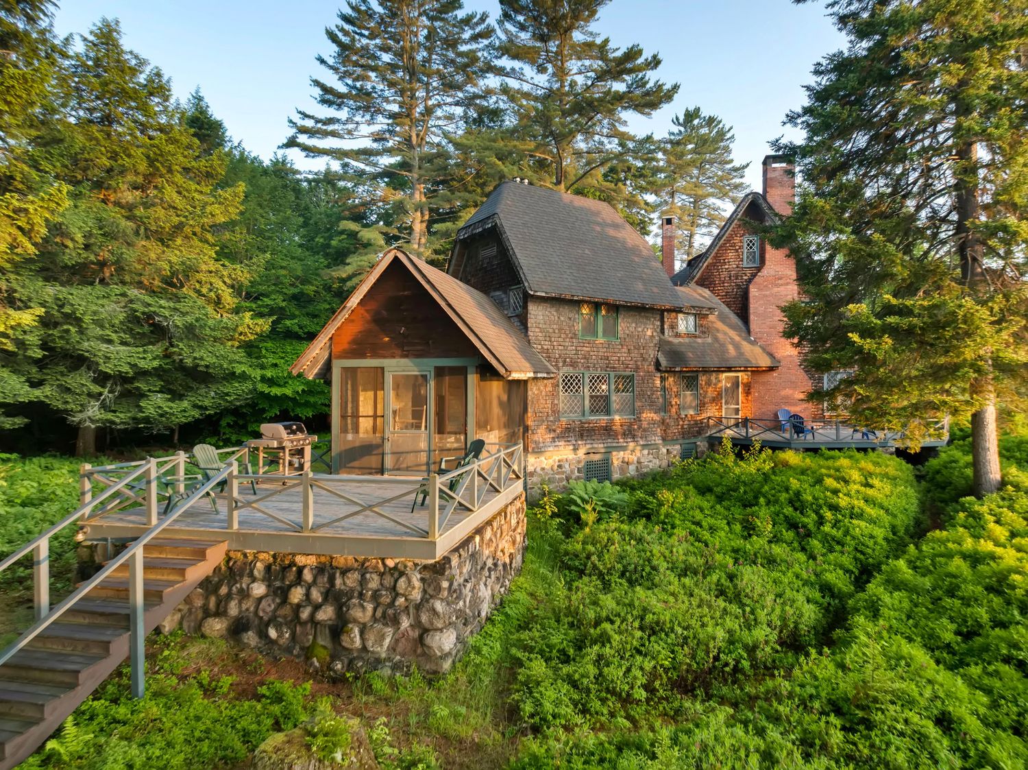 Scenic waterfront cabins nestled among evergreen trees along a rocky coastline in Maine during golden hour.