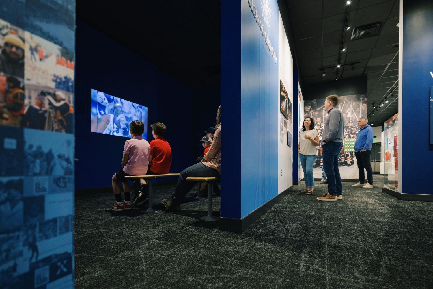 People walk through a dimly lit backstage hallway with blue walls and dark carpeting.