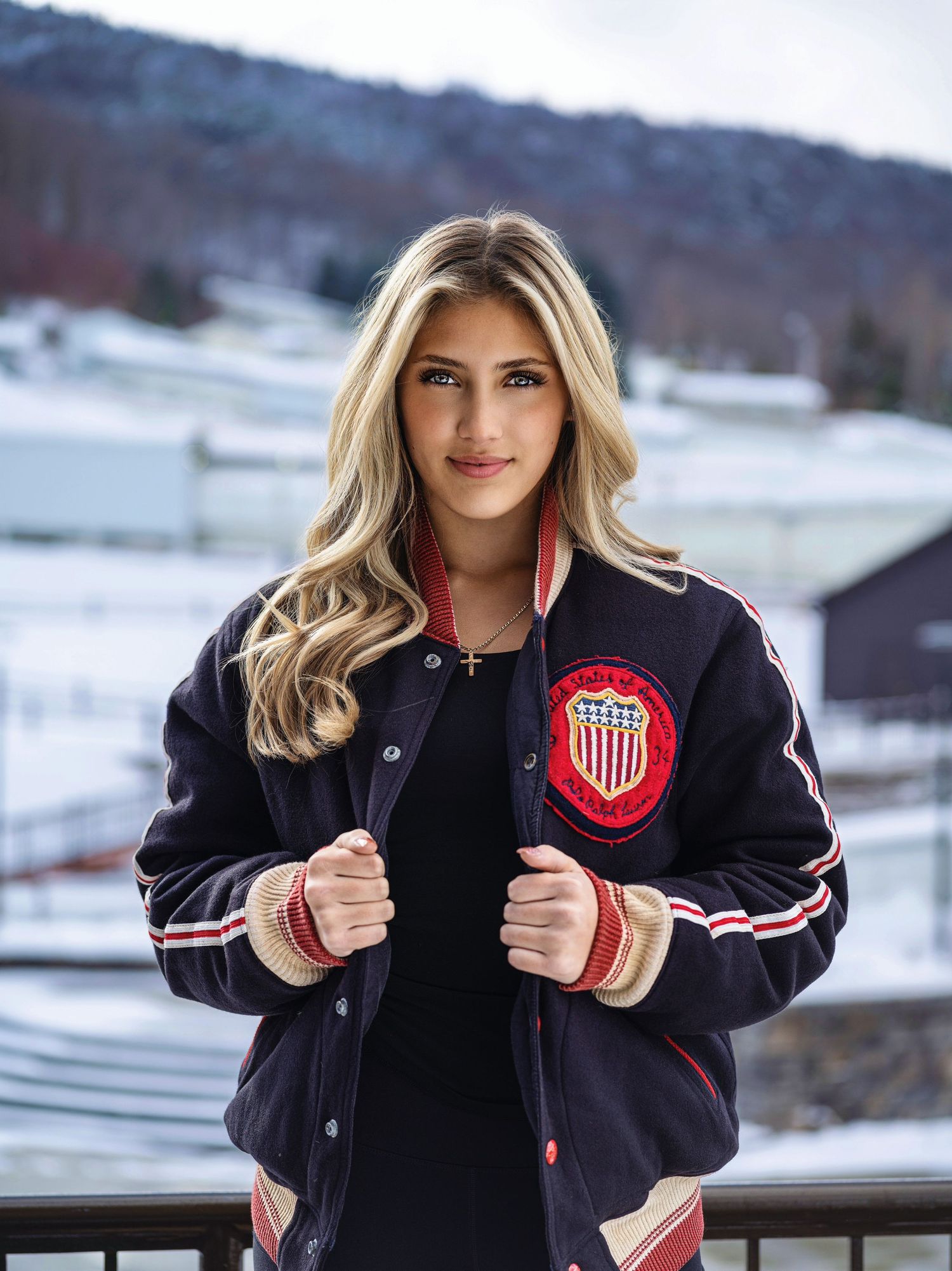 A varsity-style letterman jacket with a red and white emblem displayed against a snowy winter backdrop.