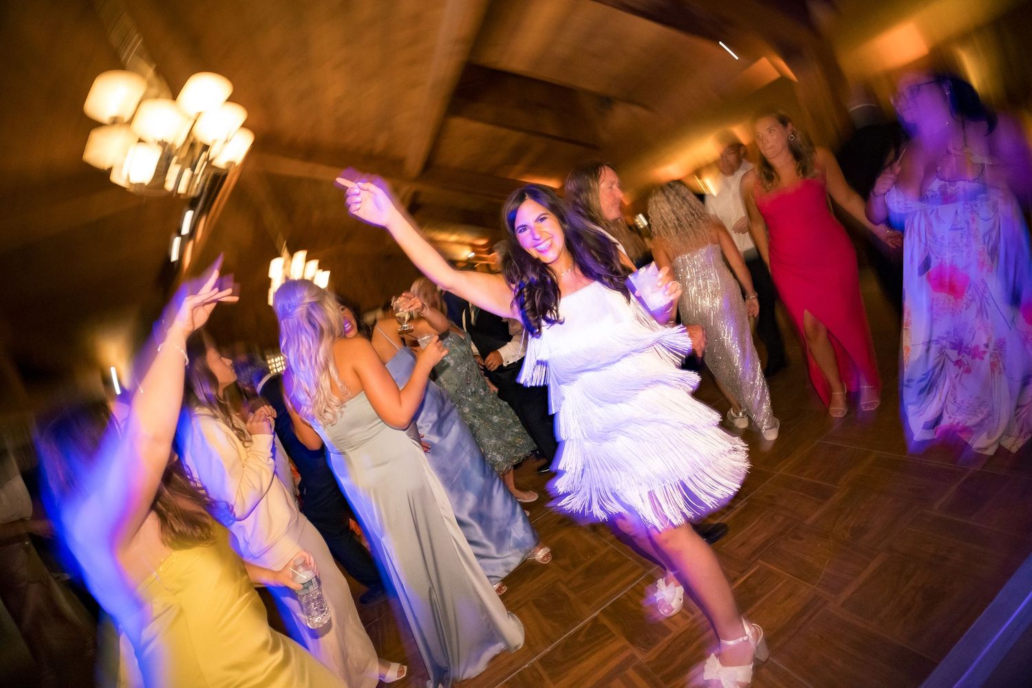 Bride dancing joyfully with guests at a lively wedding reception in an elegantly lit venue.