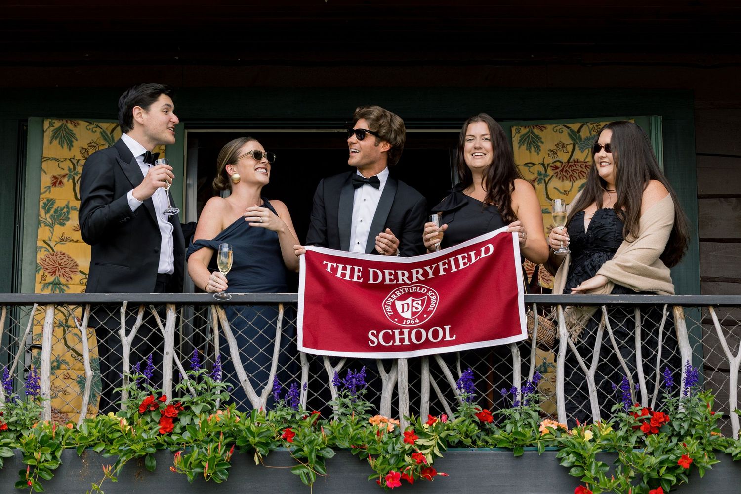 Students in formal attire hold a Derryfield School banner on a decorated balcony at a school event.