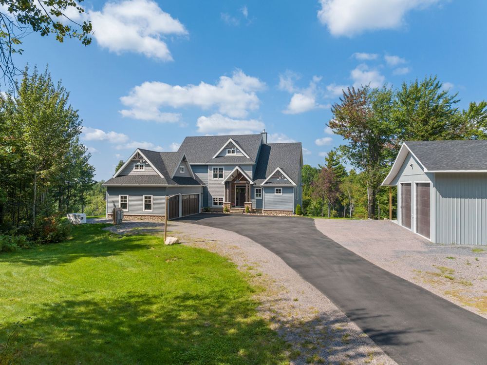 A panoramic view of a residential driveway leading to a modern house with gray siding and a well-maintained lawn.