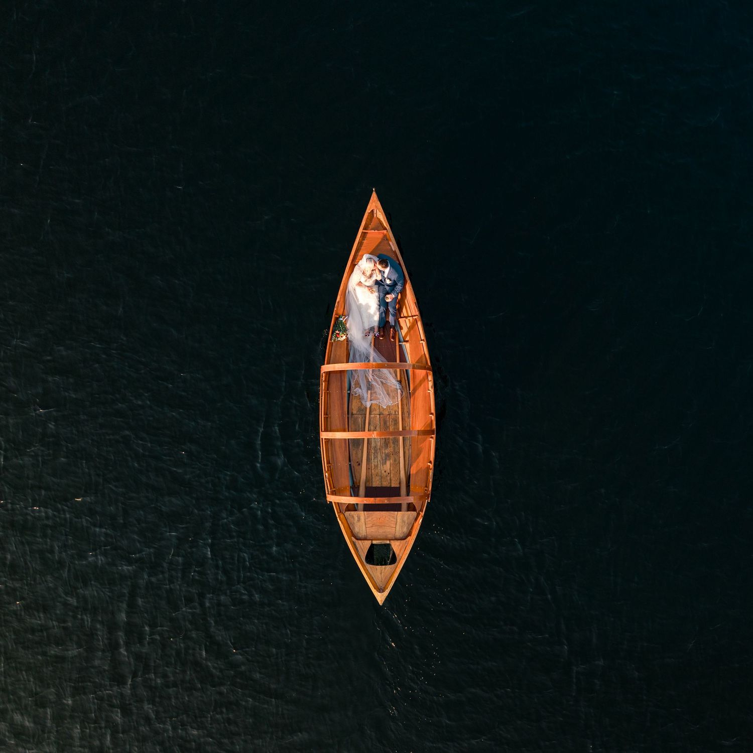 Aerial sequence showing a wooden rowboat gradually becoming smaller as it floats on dark ocean waters.