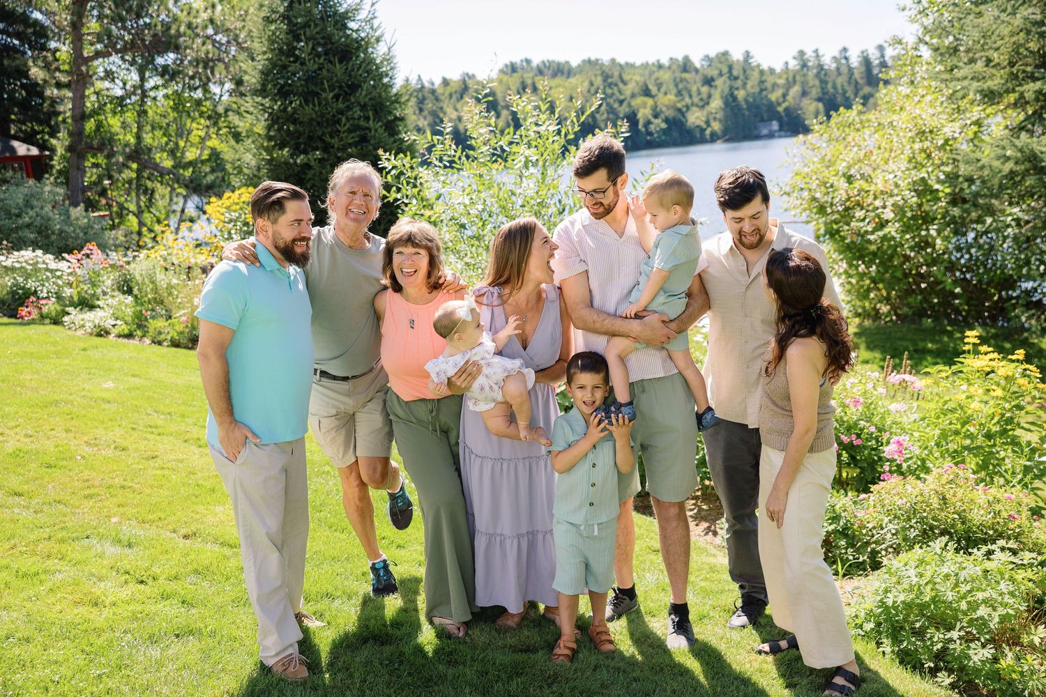 Wedding party in pastel attire laughs together while walking through a sunny garden on a summer afternoon.