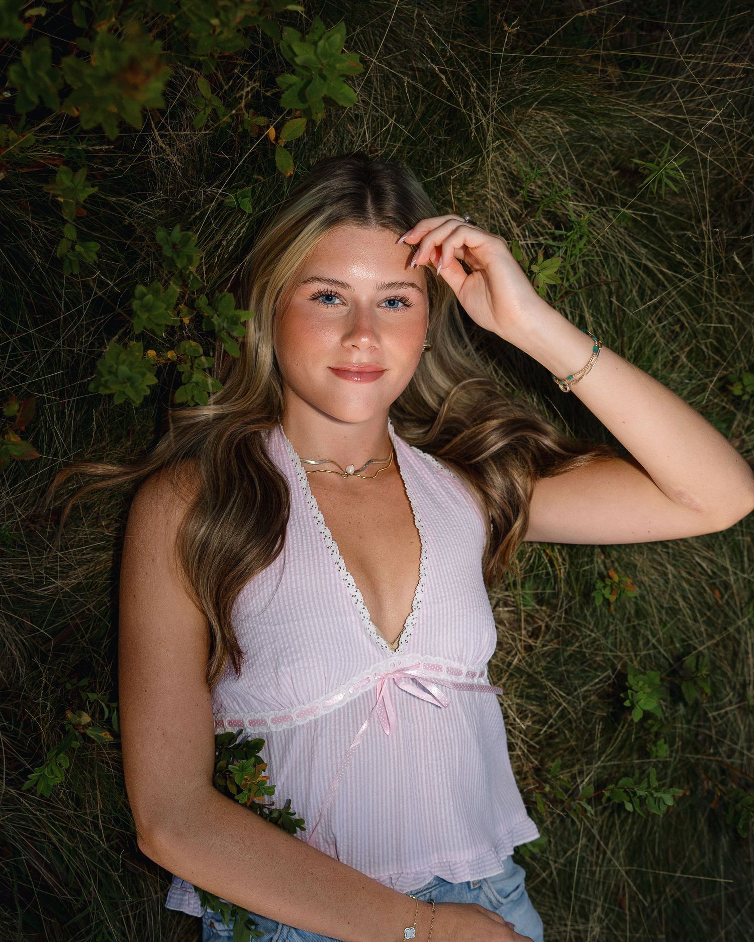A person in a white lace-trimmed top poses outdoors against a natural green foliage background.