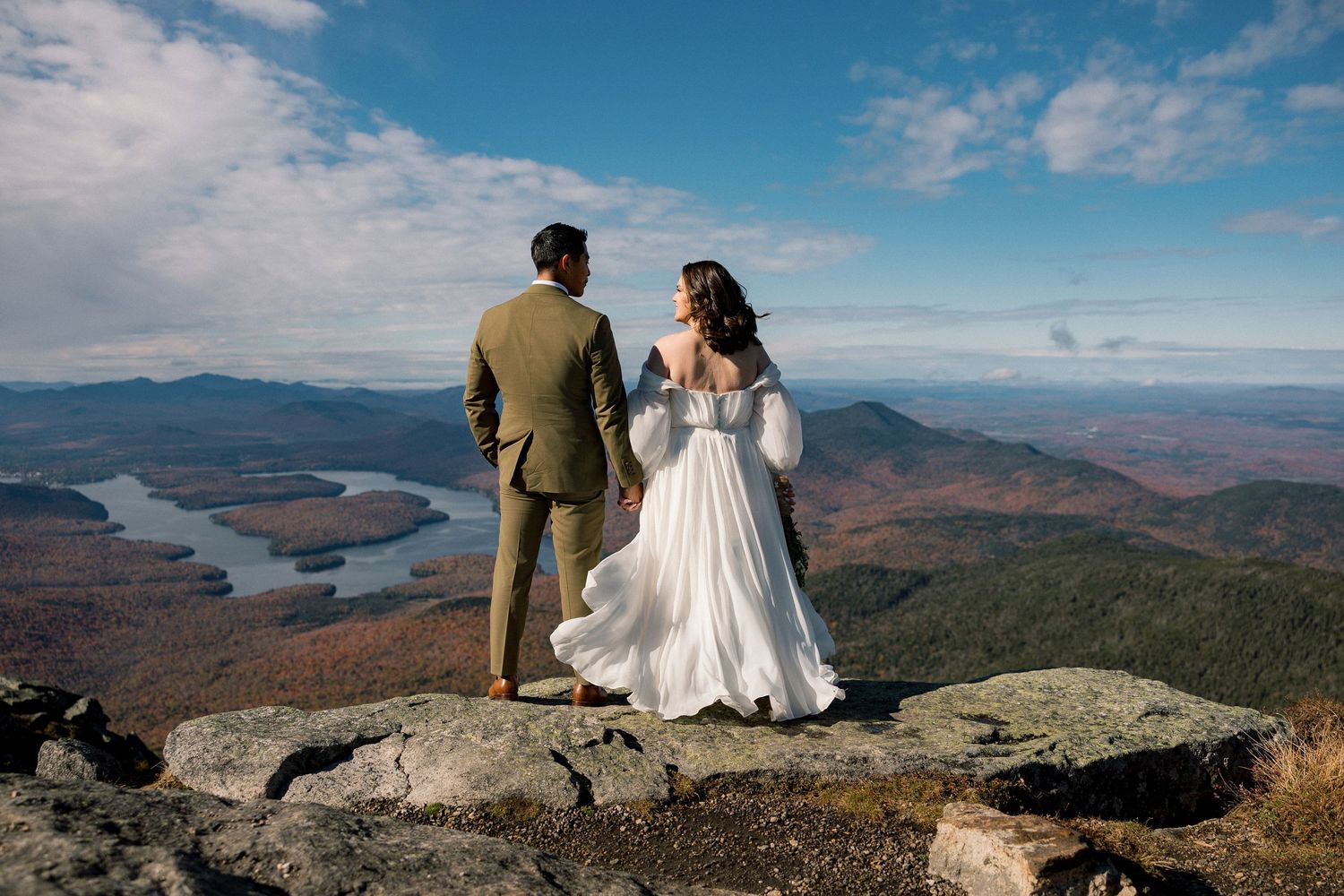 Wedding couple sitting on mountain summit overlooking scenic autumn valley landscape.