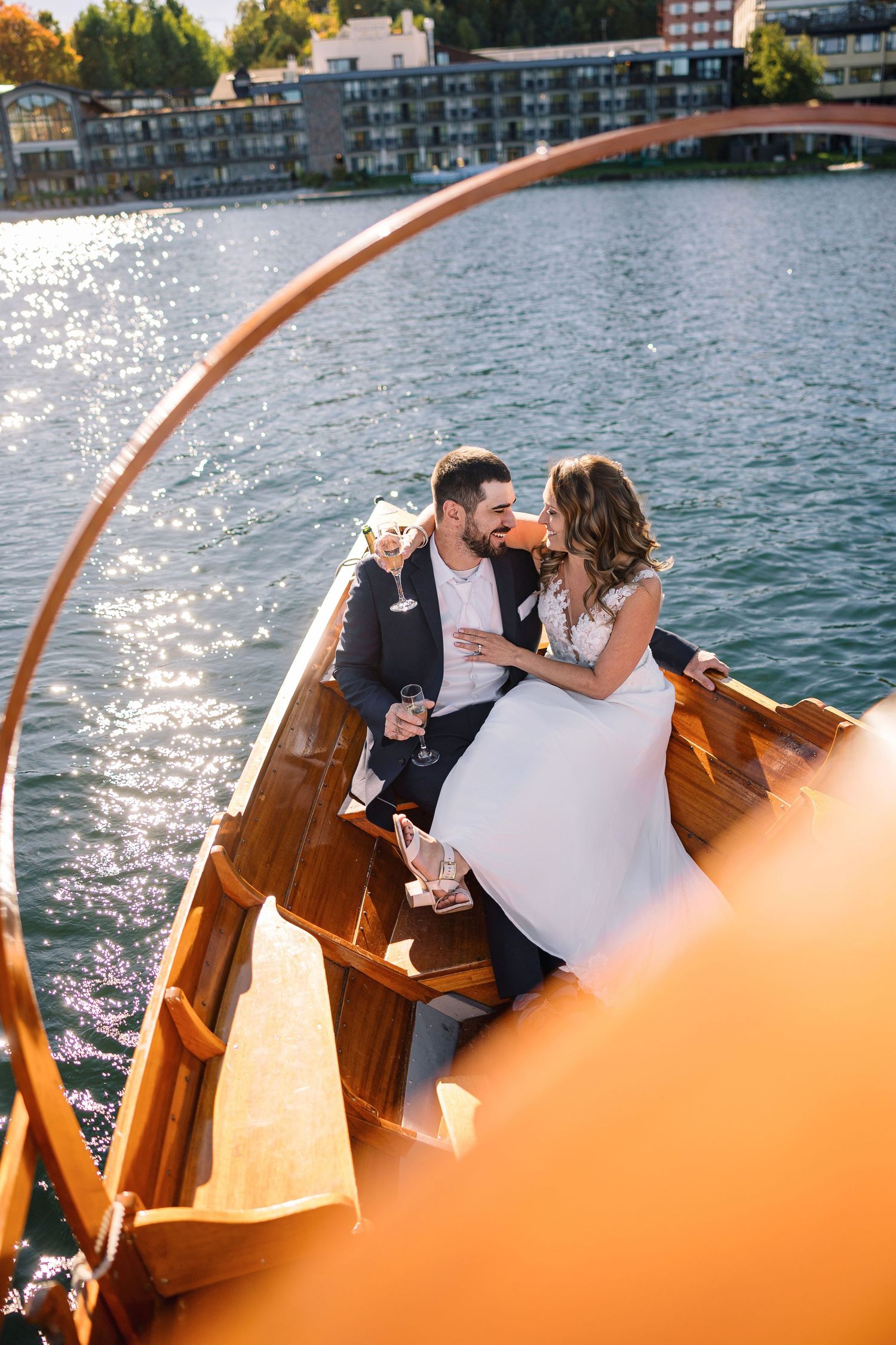 A romantic couple shares tender moments on a wooden boat against a sparkling waterfront backdrop at sunset.