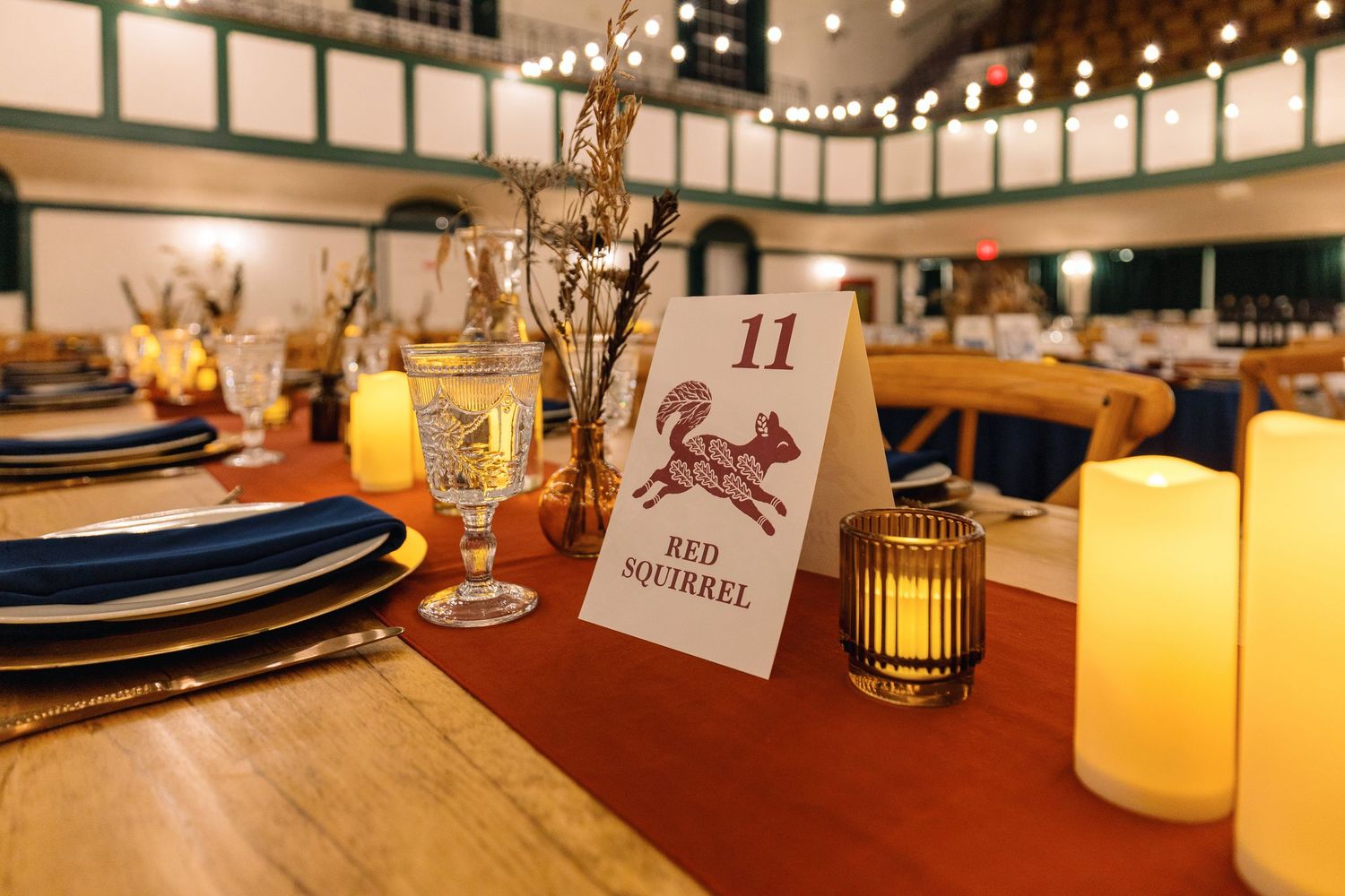 Elegant wedding reception table settings with glowing candles and place cards in a warmly lit banquet room.