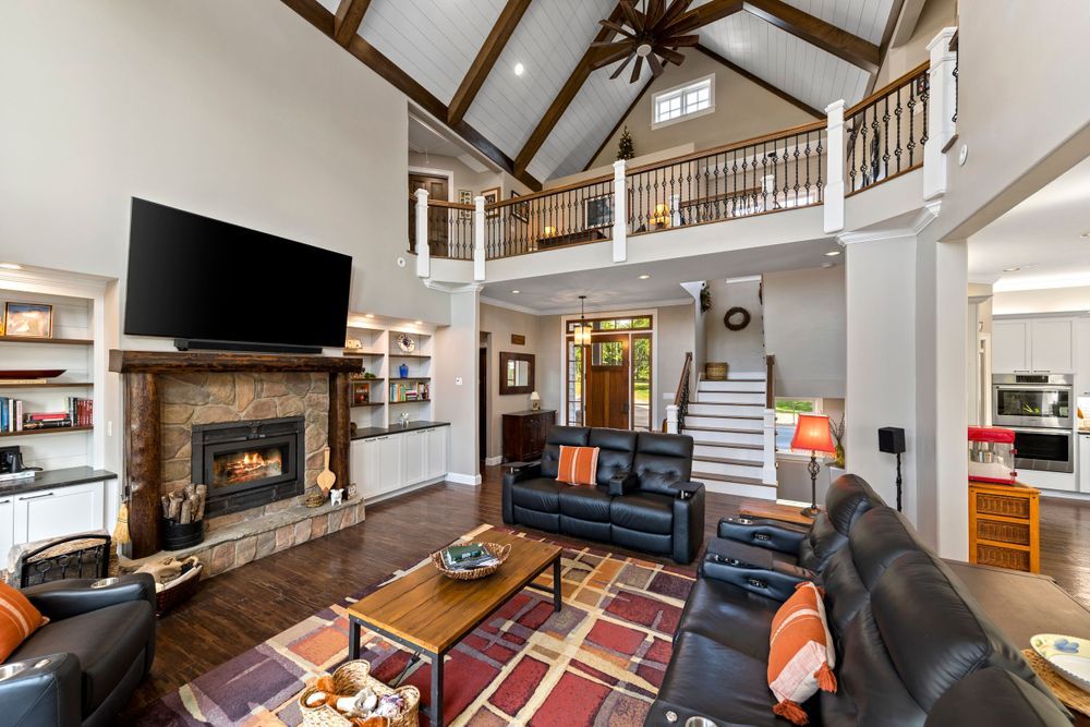 Modern living room with vaulted ceiling features a stone fireplace, leather furniture, and rustic wood accents.