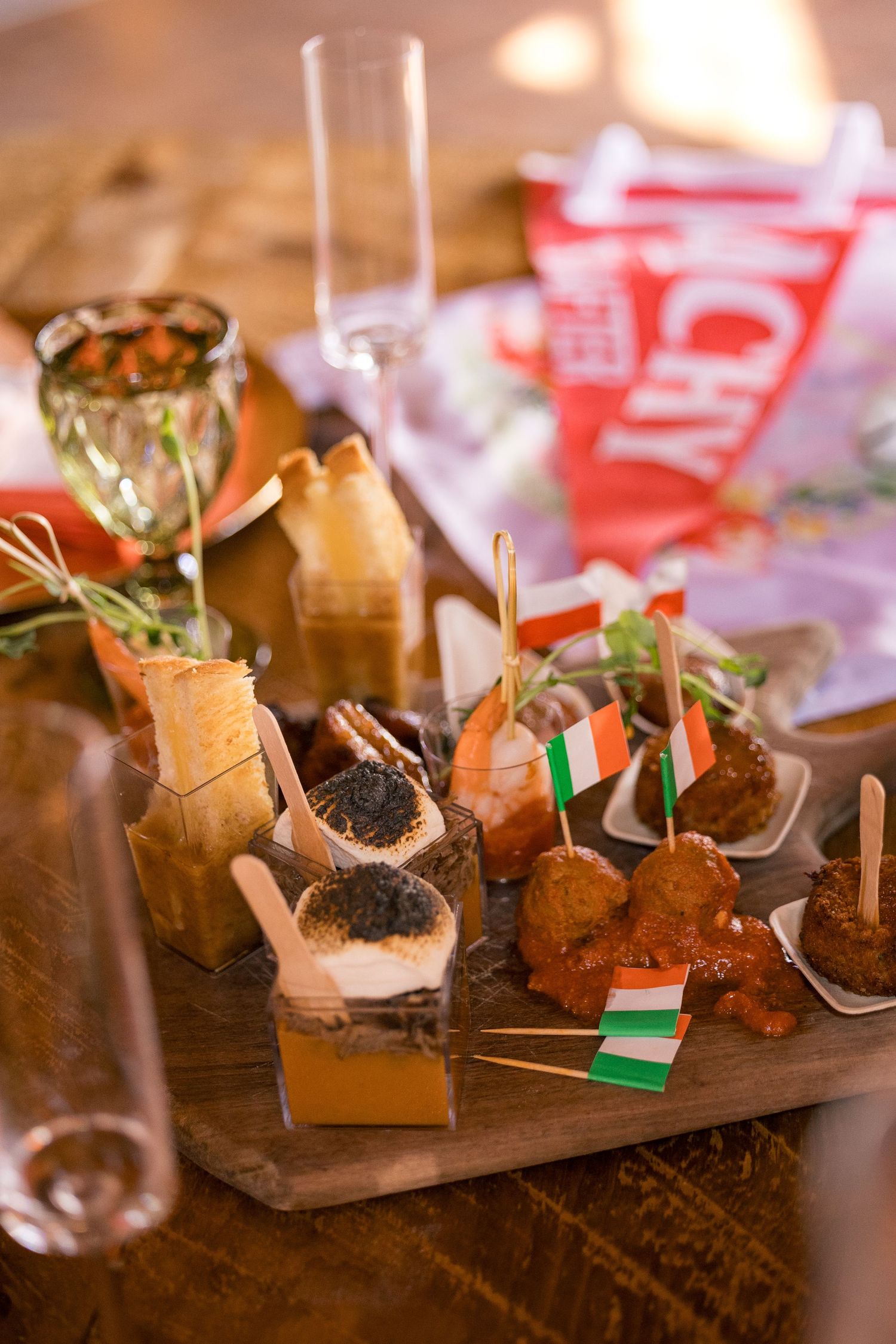 Elegant party appetizers on wooden board with Irish flags, shrimp, caviar bites, and champagne glasses at festive event.