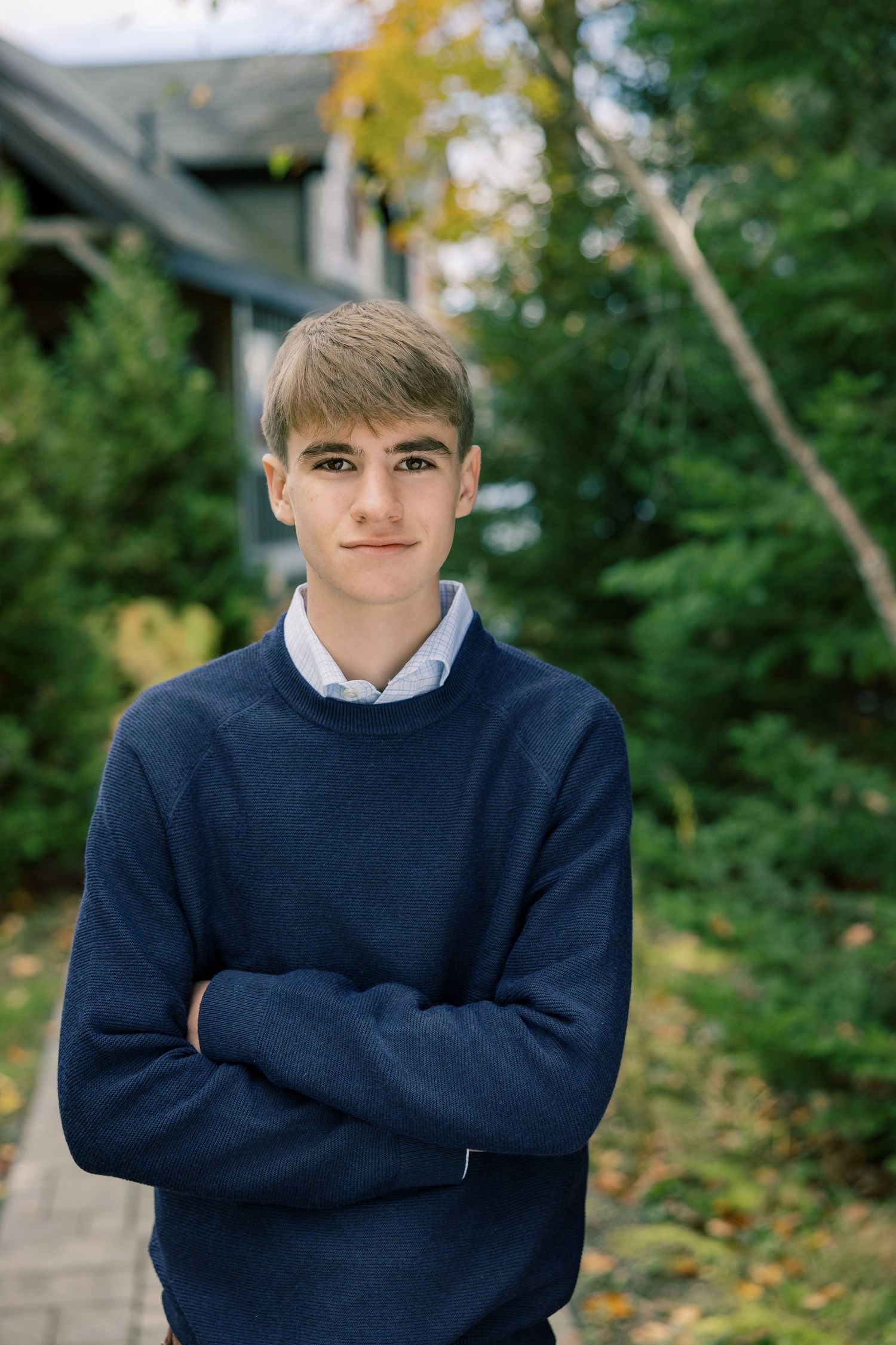 Portrait series in outdoor setting showing person wearing navy sweater and white collared shirt against green foliage.