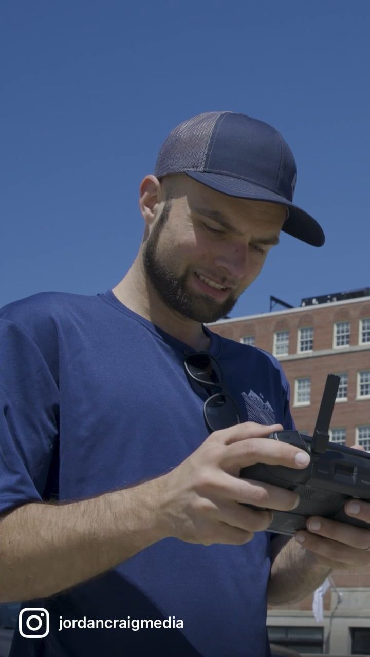 Person in navy blue shirt and baseball cap smiles while looking down at handheld device outdoors.