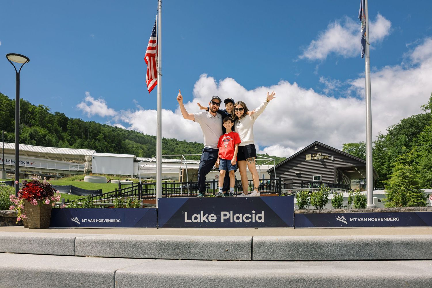 Athletes pose on the Olympic ski jumping platform at Lake Placid's historic winter sports complex on a sunny summer day.