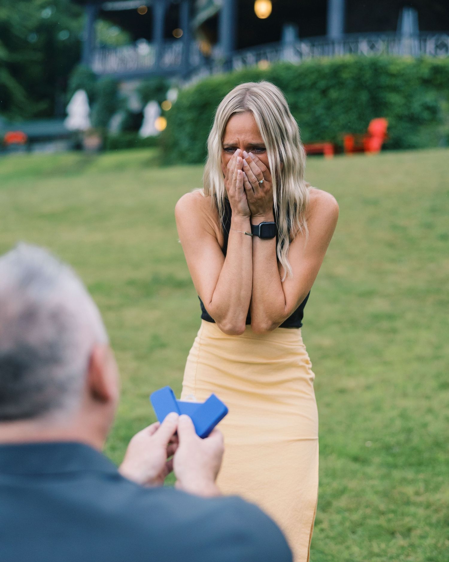 An emotional proposal reaction on a lawn with outdoor lighting in the background.
