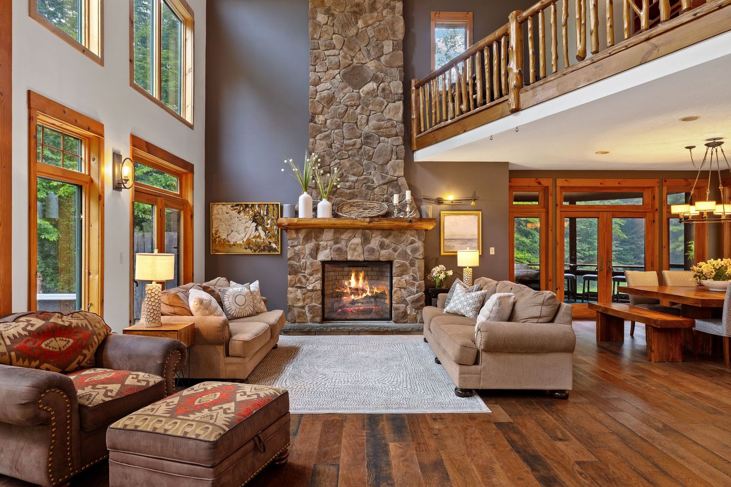 Luxurious mountain home living room with tall stone fireplace, hardwood floors and rustic decor beneath vaulted ceilings.