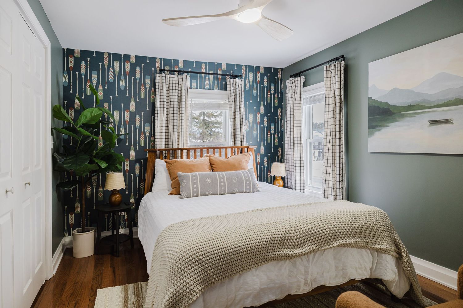 Modern bedroom with blue geometric wallpaper accent wall, white bedding, and large windows letting in natural light.