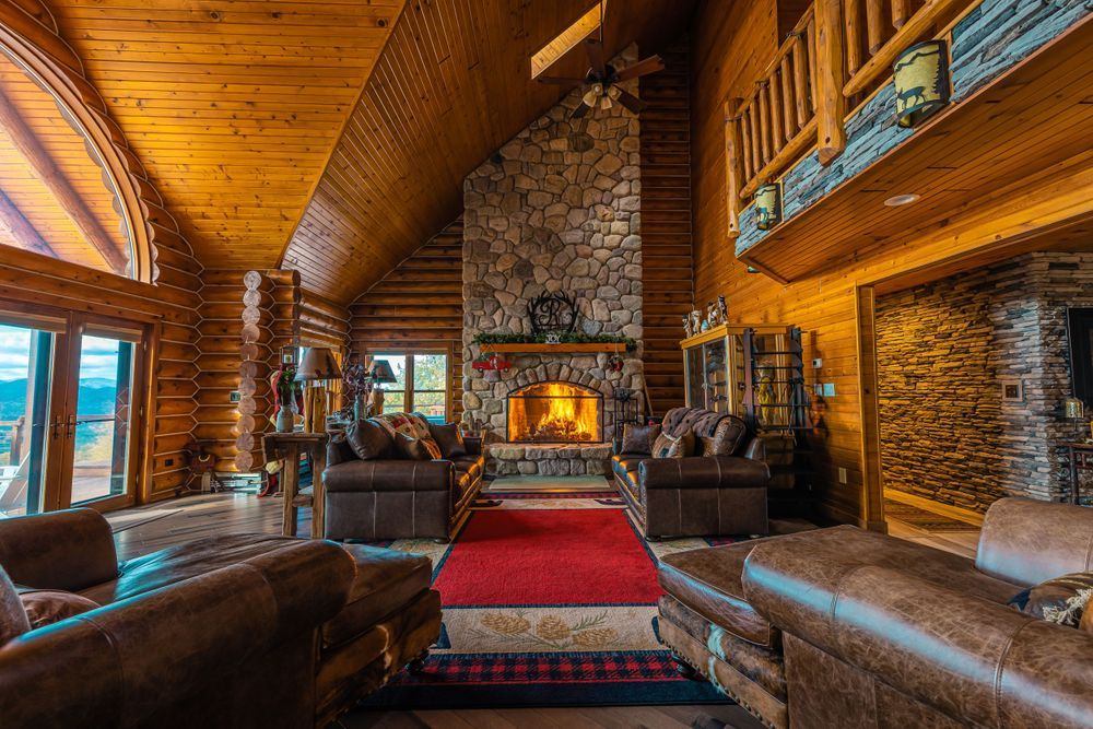Cozy rustic cabin interior with stone fireplace, wood beams, and warm lighting creating an inviting mountain retreat atmosphere.