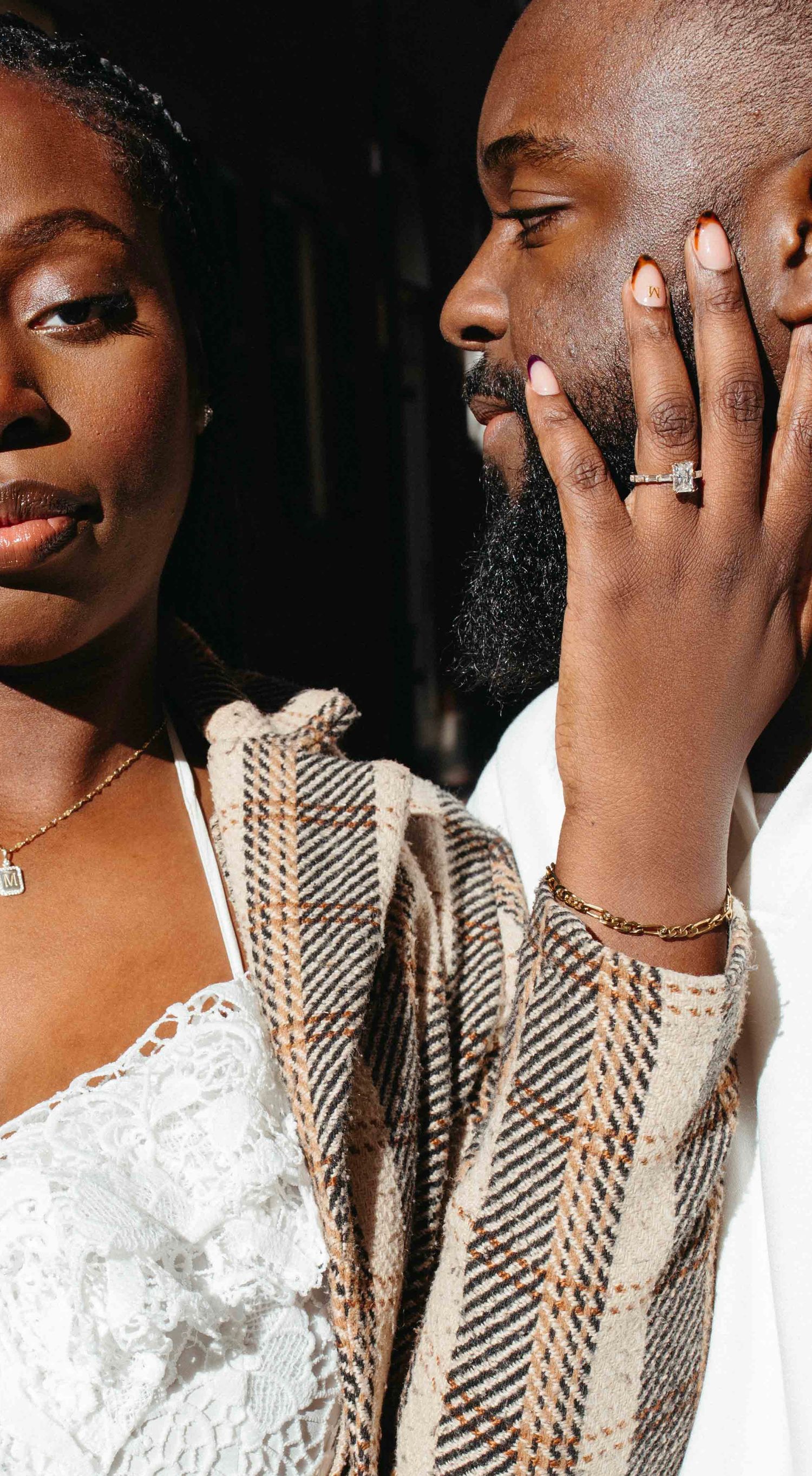 Close-up portrait of person wearing white lace and striped pattern clothing while touching their face with ring-adorned hand.