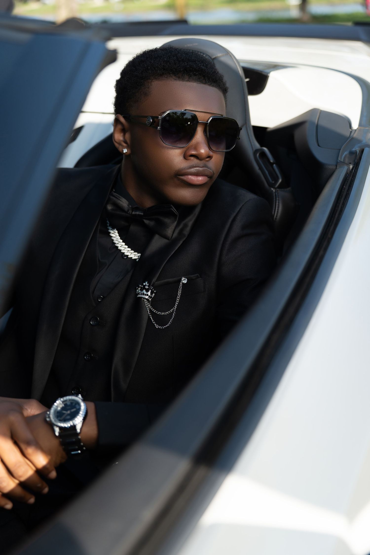 A person wearing sunglasses and dark clothing sits in the driver's seat of a white car in a series of connected photos.