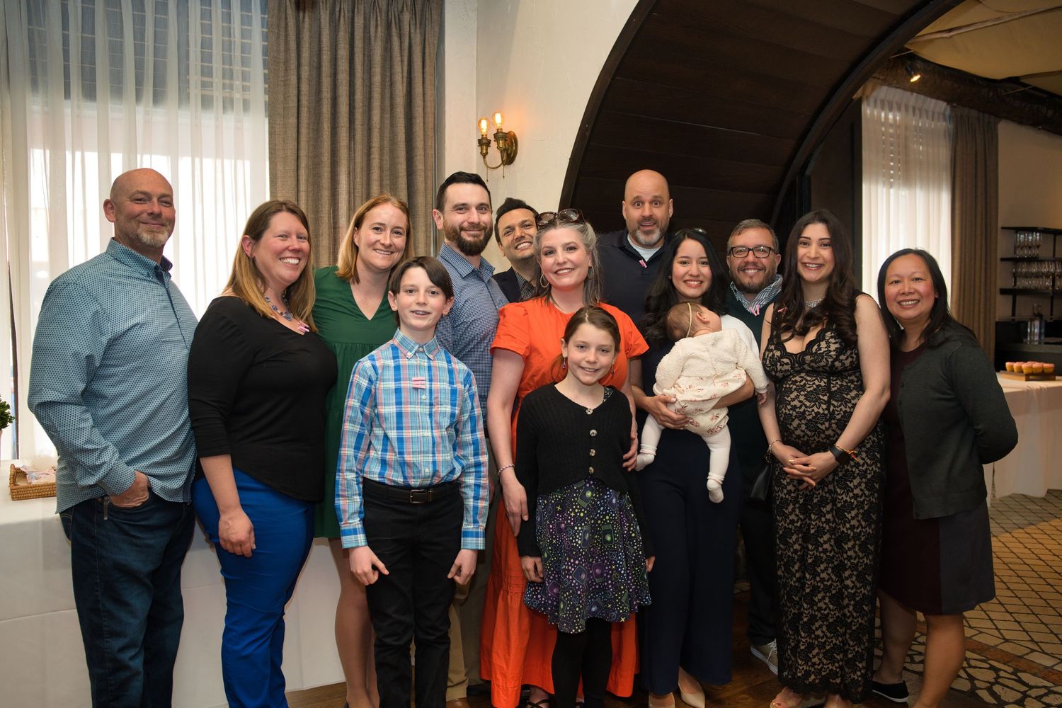 A large family group poses together for a formal portrait in a well-lit indoor setting with curtains in the background.