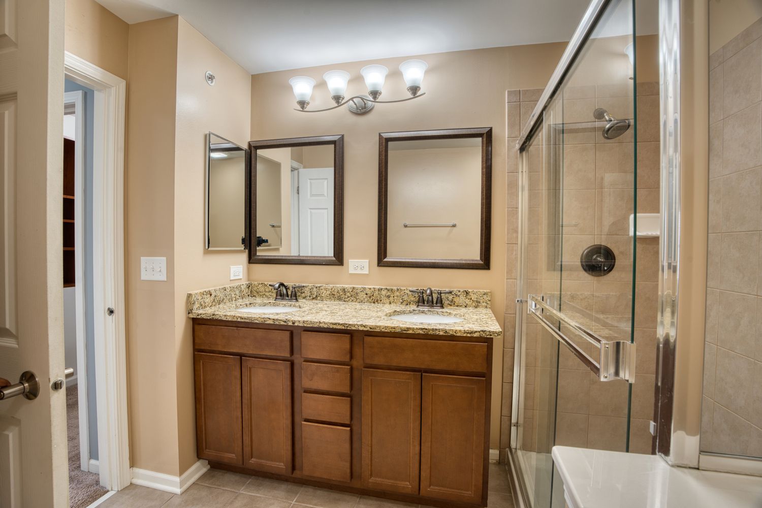 Modern bathroom interior with granite countertops, wooden cabinets, and chrome fixtures.