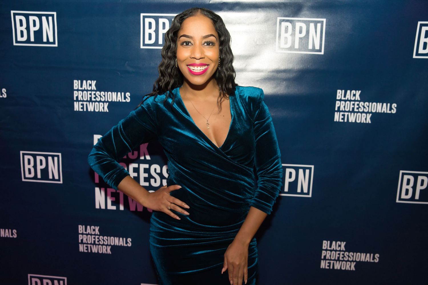 A person wearing a dark blue velvet dress poses against a backdrop with BPN logos at a media event.