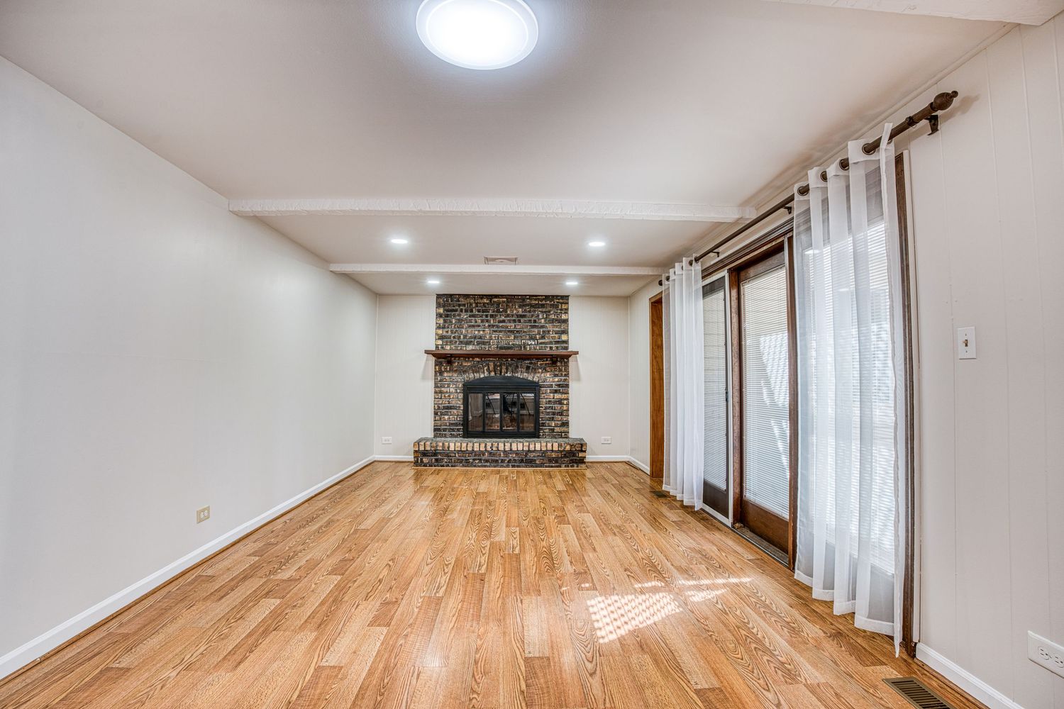 Spacious room with hardwood flooring, ceiling fan, and large windows providing natural light.