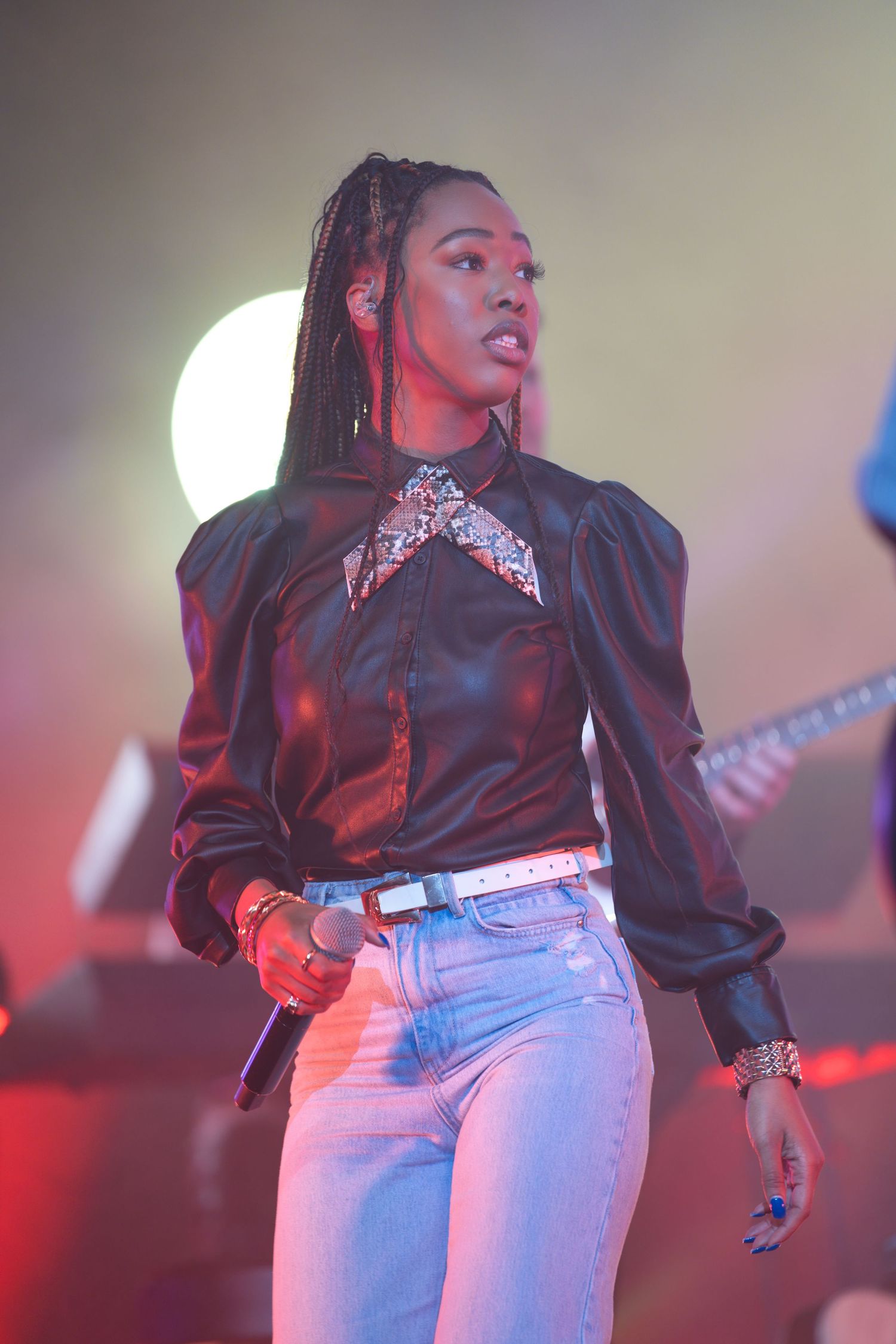 Performer on stage wearing black top and light jeans under colorful stage lighting.