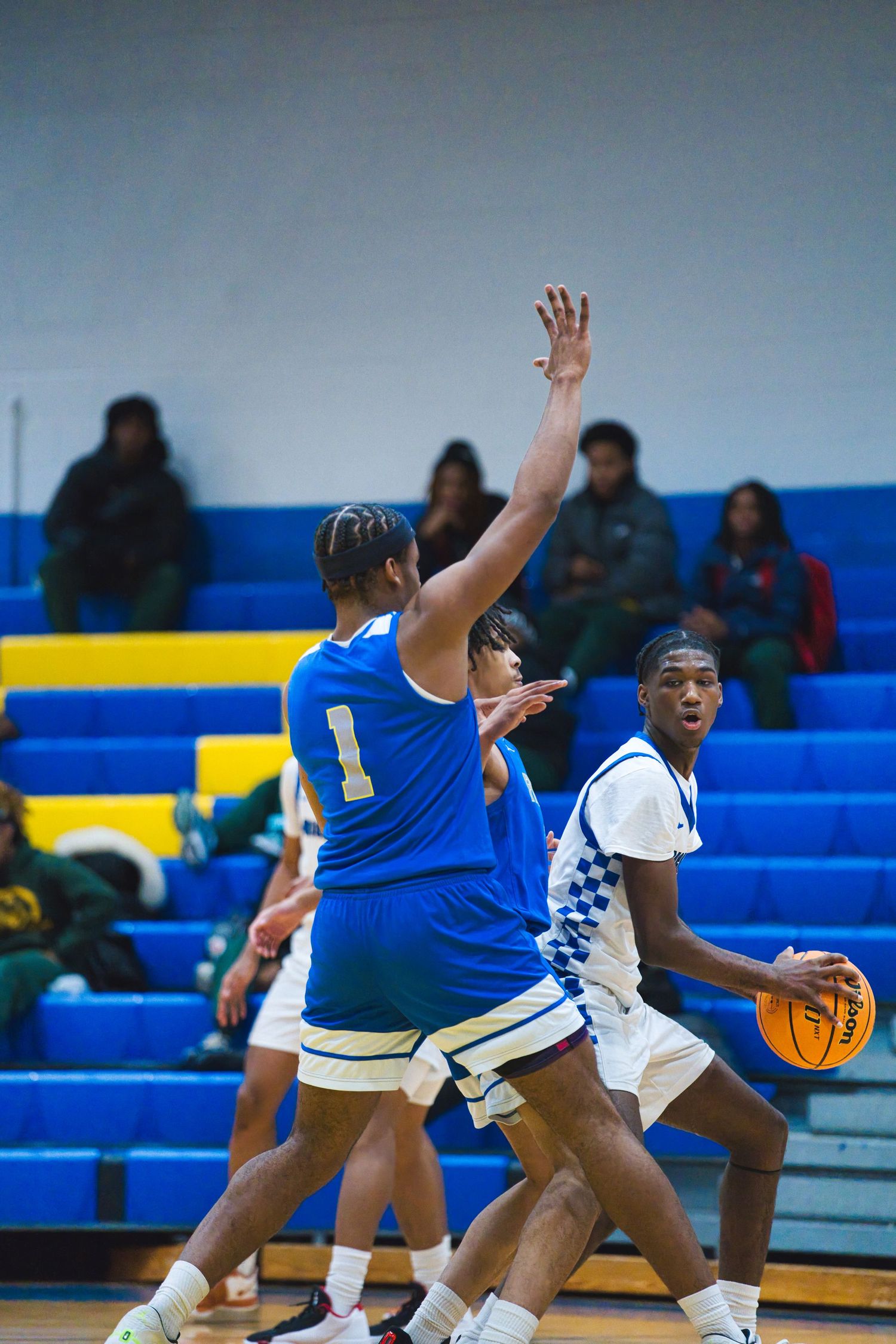 Basketball players compete for possession of the ball during an intense game between teams in blue and white uniforms.