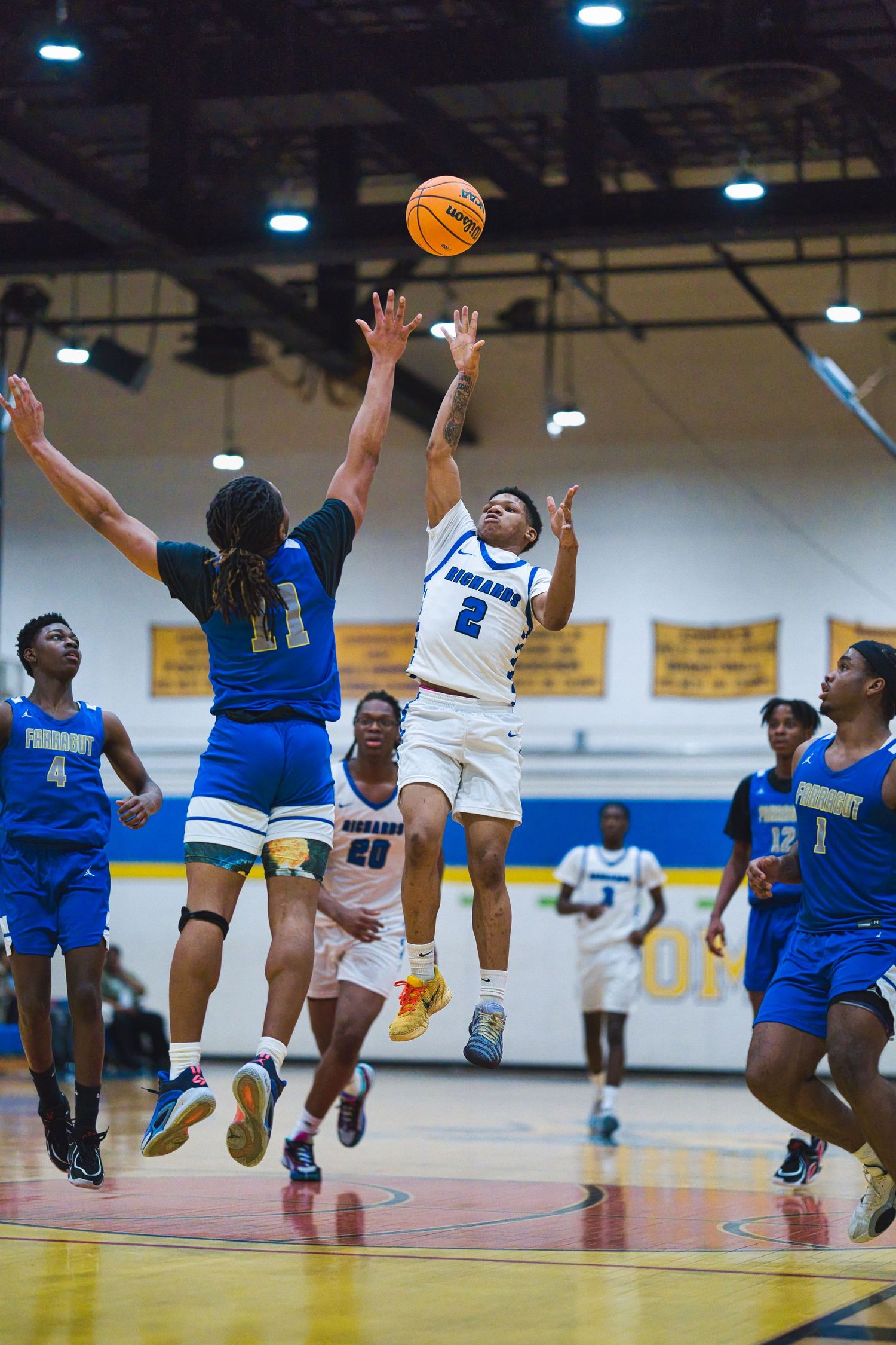 Basketball players leap high to compete for a rebound during an intense game in a school gymnasium.