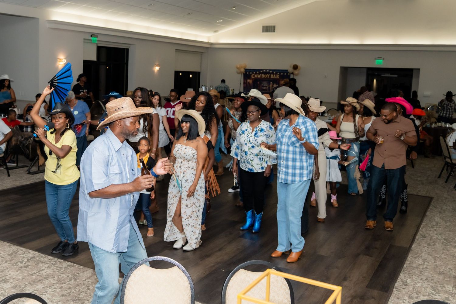 A group of people dancing and socializing at a community event in an indoor venue with hardwood floors.