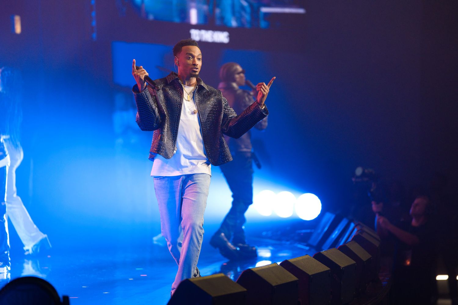 Concert performers on stage with dramatic blue lighting and silhouettes visible in the background.