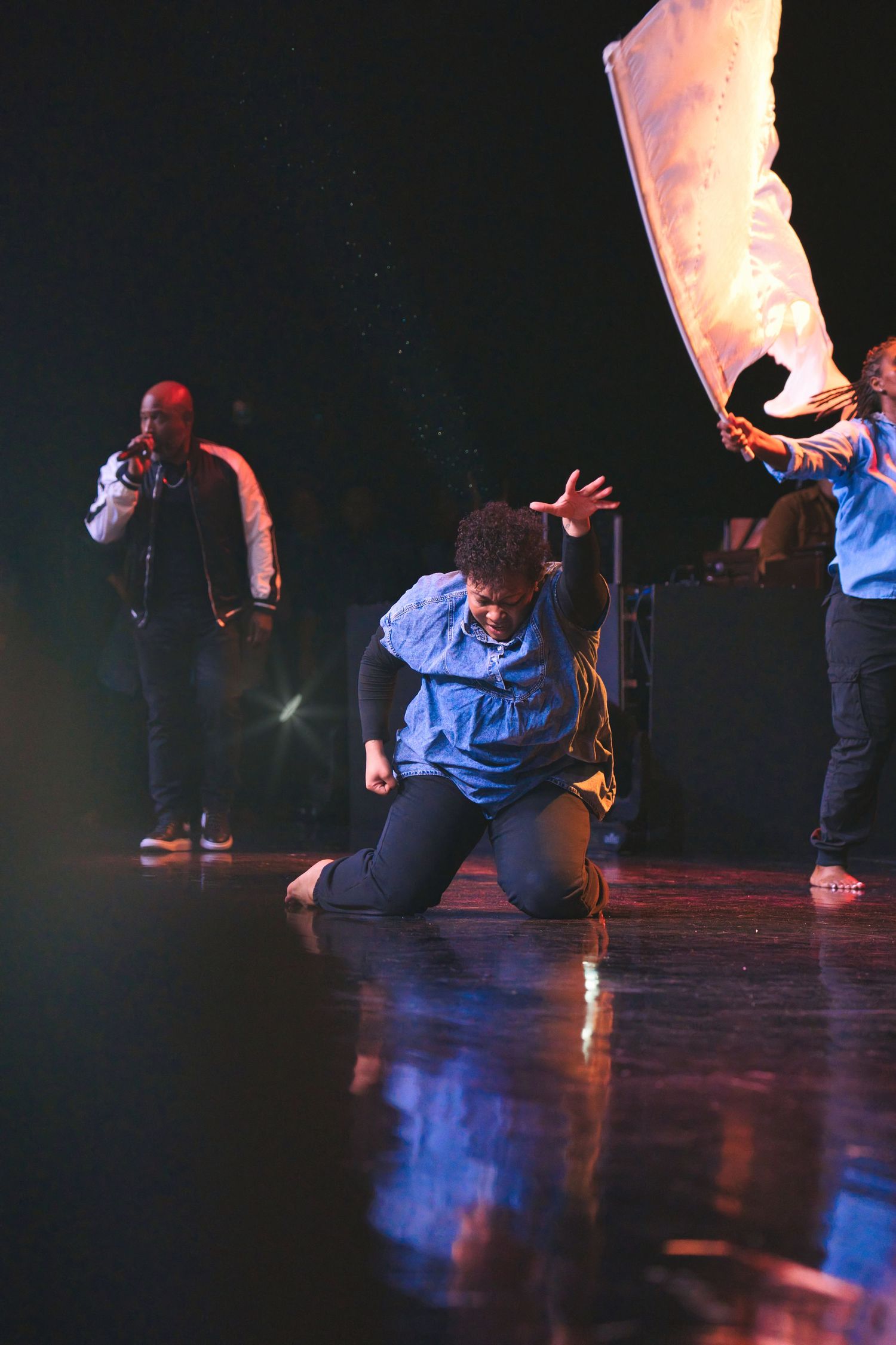 Dance performance on reflective stage floor with dramatic lighting.