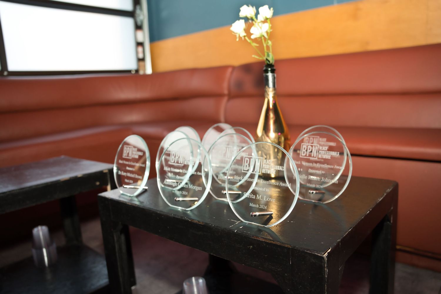 Empty wine glasses sit on a dark wooden table in a restaurant setting with orange walls in the background.