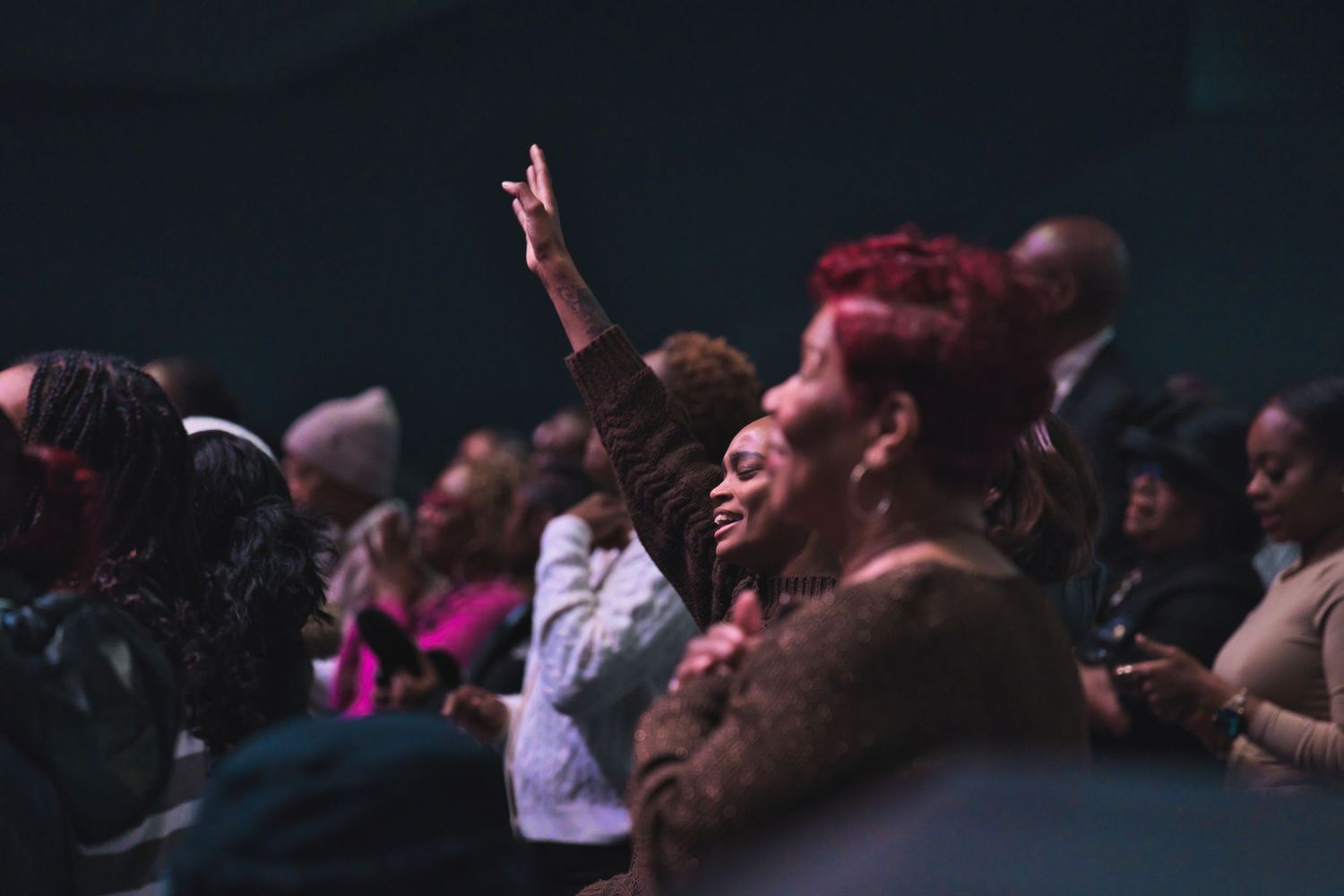 Audience members at a concert raising their hands in worship.