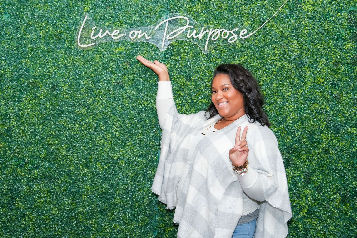 People posing in front of a green hedge wall backdrop wearing white outfits at a special event.