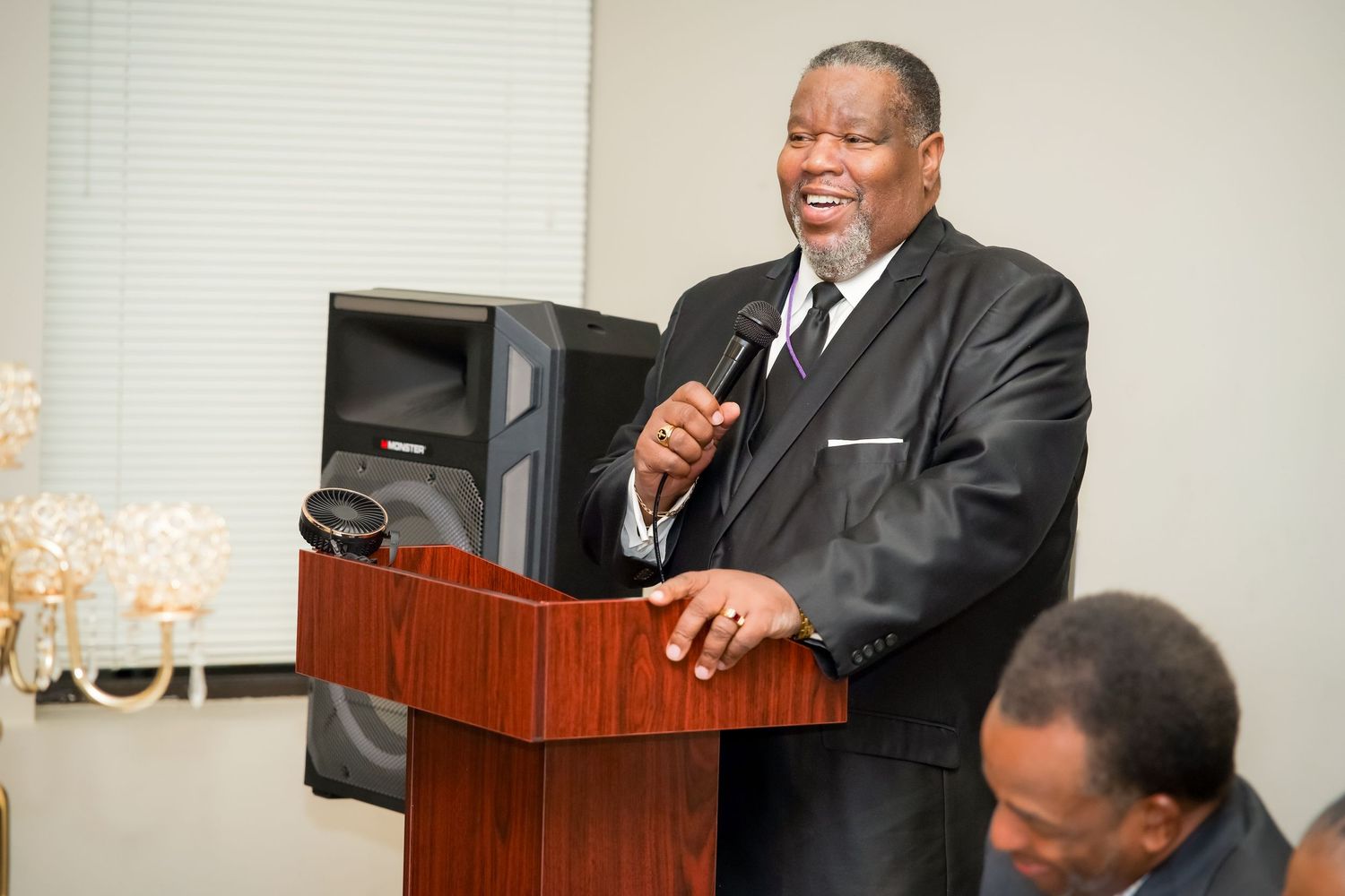 Professional speaker in a dark suit gestures while giving a presentation at a wooden podium.