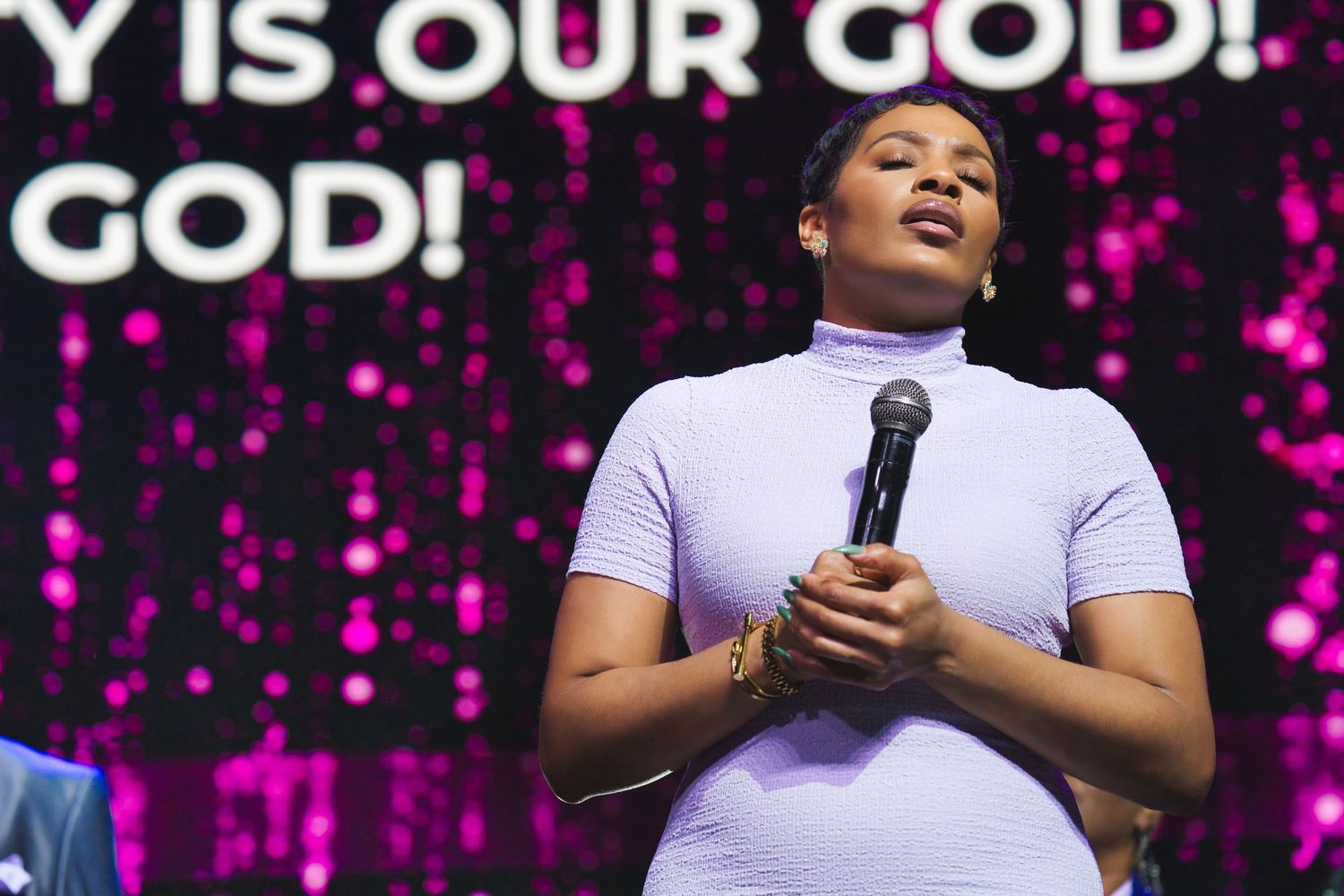 People worshipping and singing during a vibrant church service with pink lighting and stage effects.