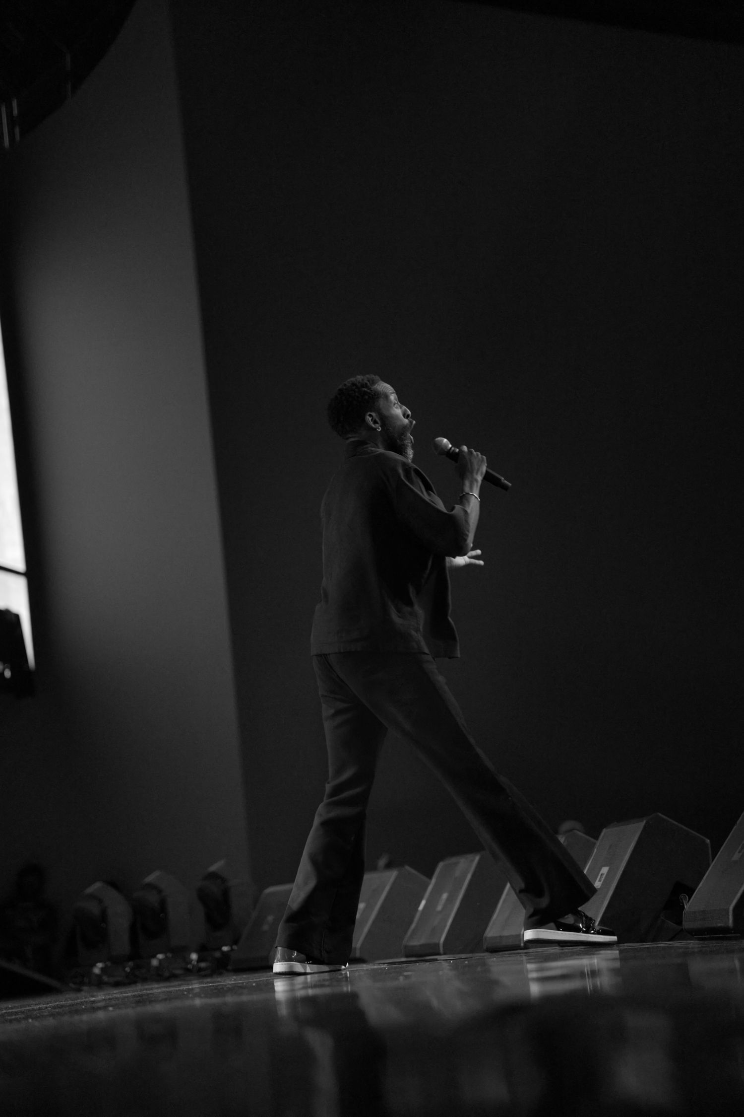 Dramatic black and white silhouette of a performer on stage with chairs lined up in the background.