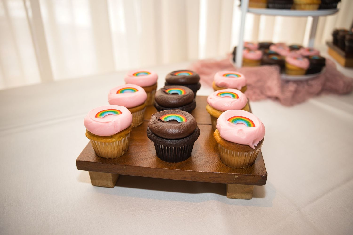 Pink and chocolate cupcakes with frosting displayed on a wooden serving tray at a special event.