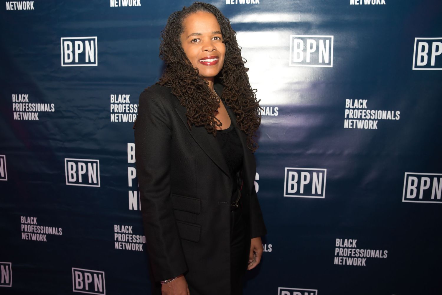 A person smiles while posing in front of a black backdrop with BPN logos at a professional event.