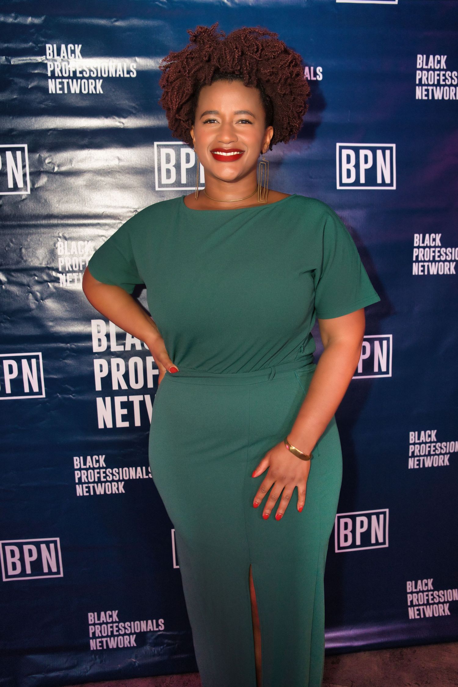 Person in emerald green dress poses confidently against Black Professionals Network backdrop at networking event.