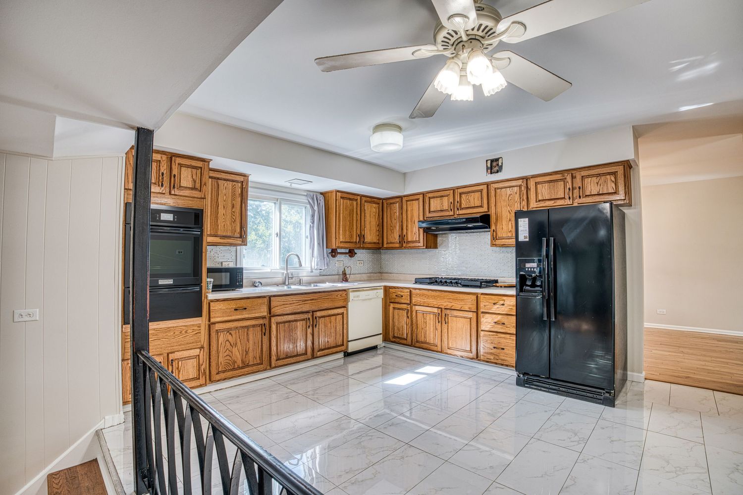 Modern kitchen with oak cabinets, black appliances, and tiled flooring opening to dining area.