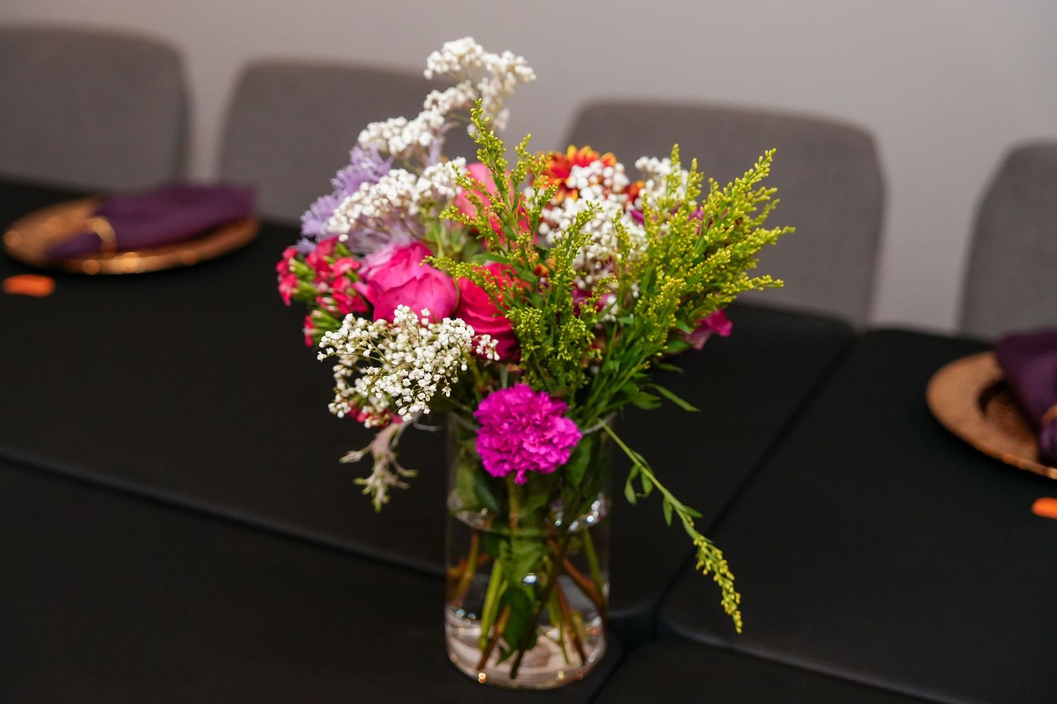A colorful floral arrangement with pink carnations and white baby's breath in a clear glass vase on a dark table.