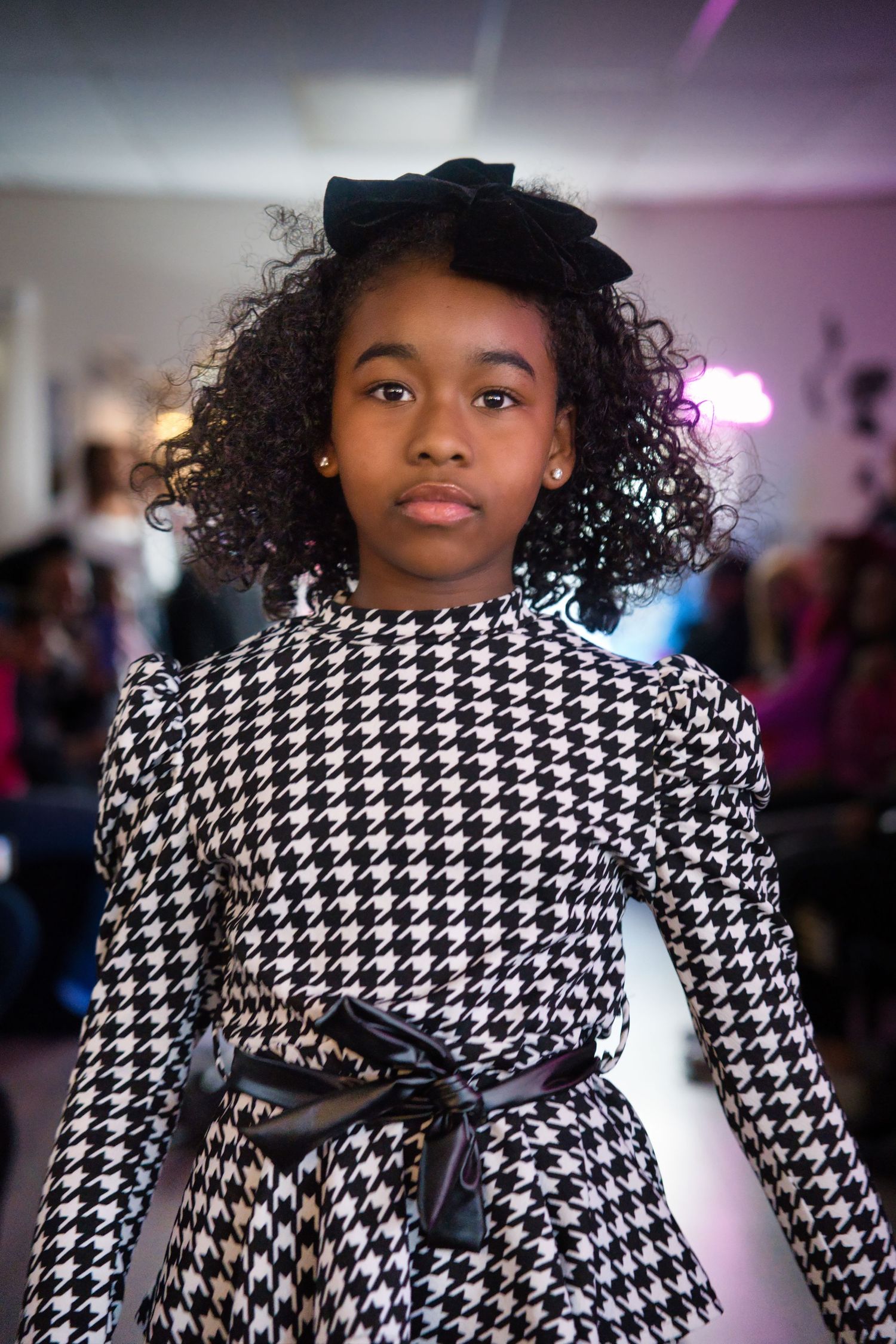 Model showcases elegant black and white houndstooth dress with bow belt on runway.