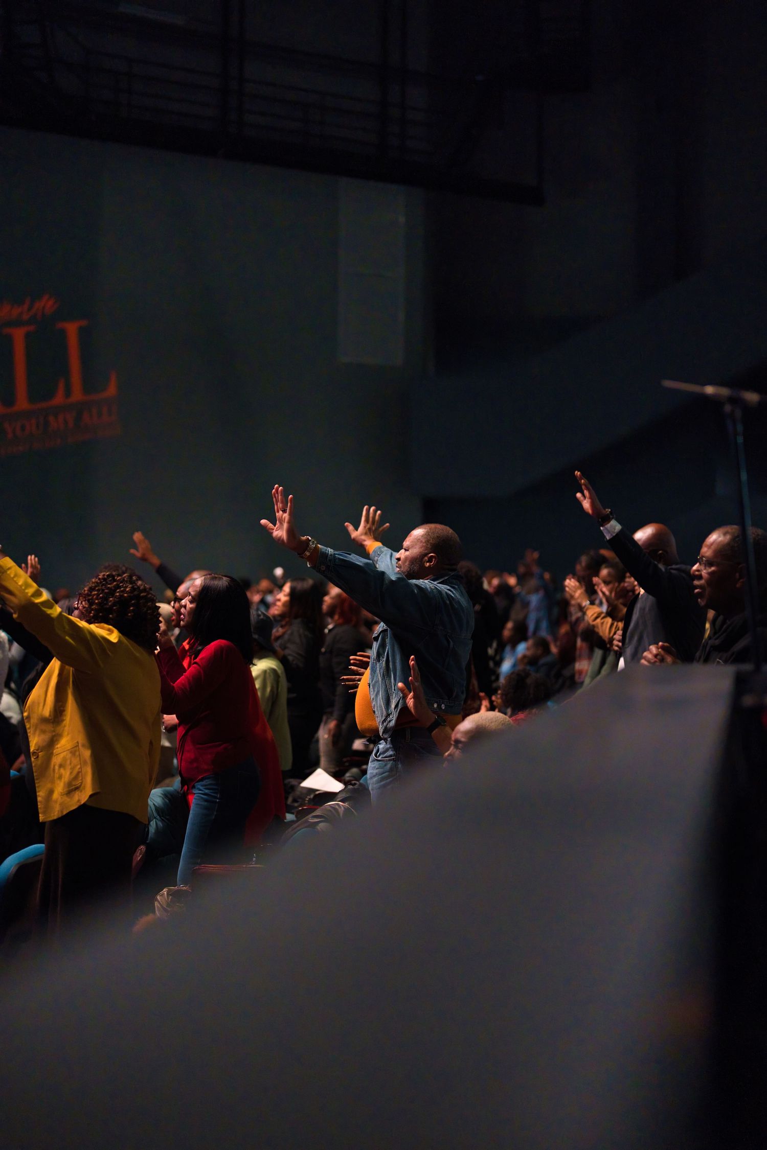 Dark concert venue with silhouetted crowd raising hands during performance.