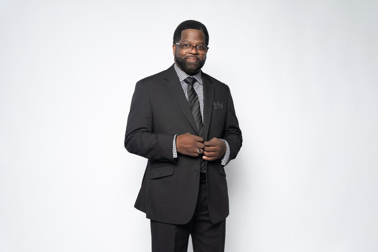 Professional portrait of person in dark suit adjusting tie against white background.